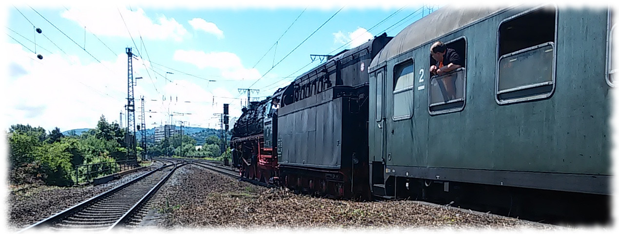 Sonderzug mit Dampflok 01 1066 von hinten im Bahnhof von Koblenz-Lützel, im Vordergrund alter Reisezugwagen, aus dem jemand aus dem geöffneten Fenster guckt. 